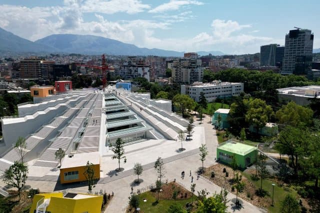 Aerial view of the Pyramid of Tirana and the city skyline by day.