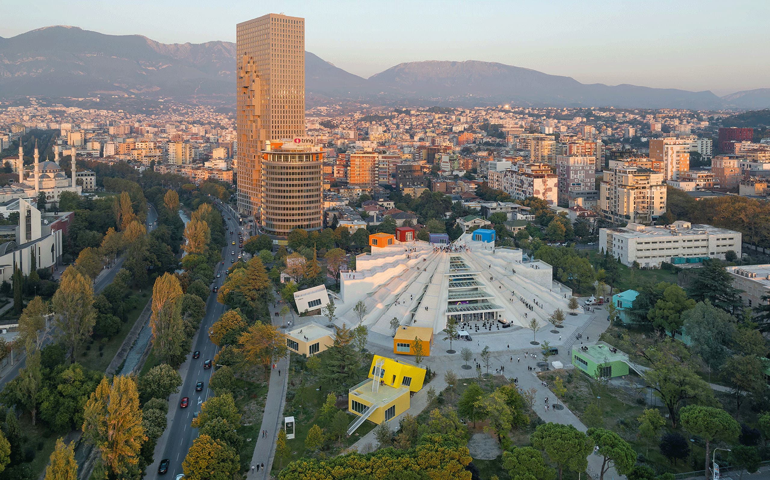 Aerial view of the Pyramid of Tirana and Tirana's skyline at golden hour.